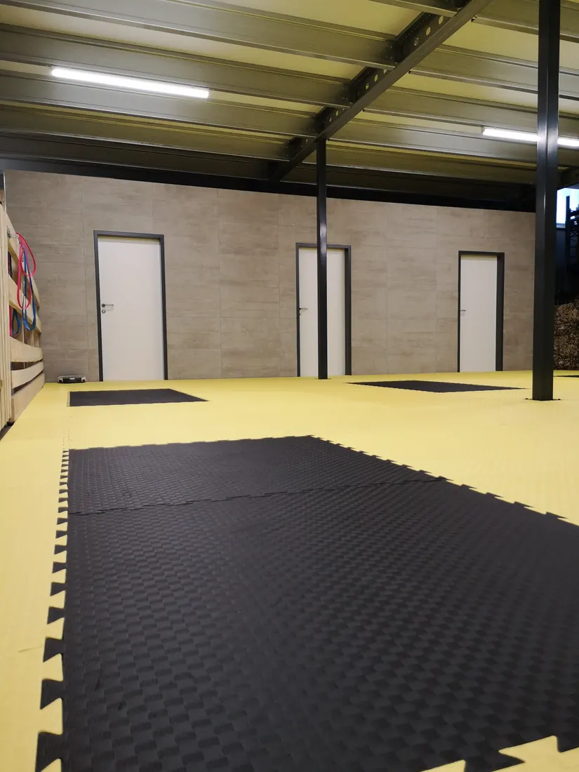 Indoorhalle mit gelbem Boden und Trainingsmatten